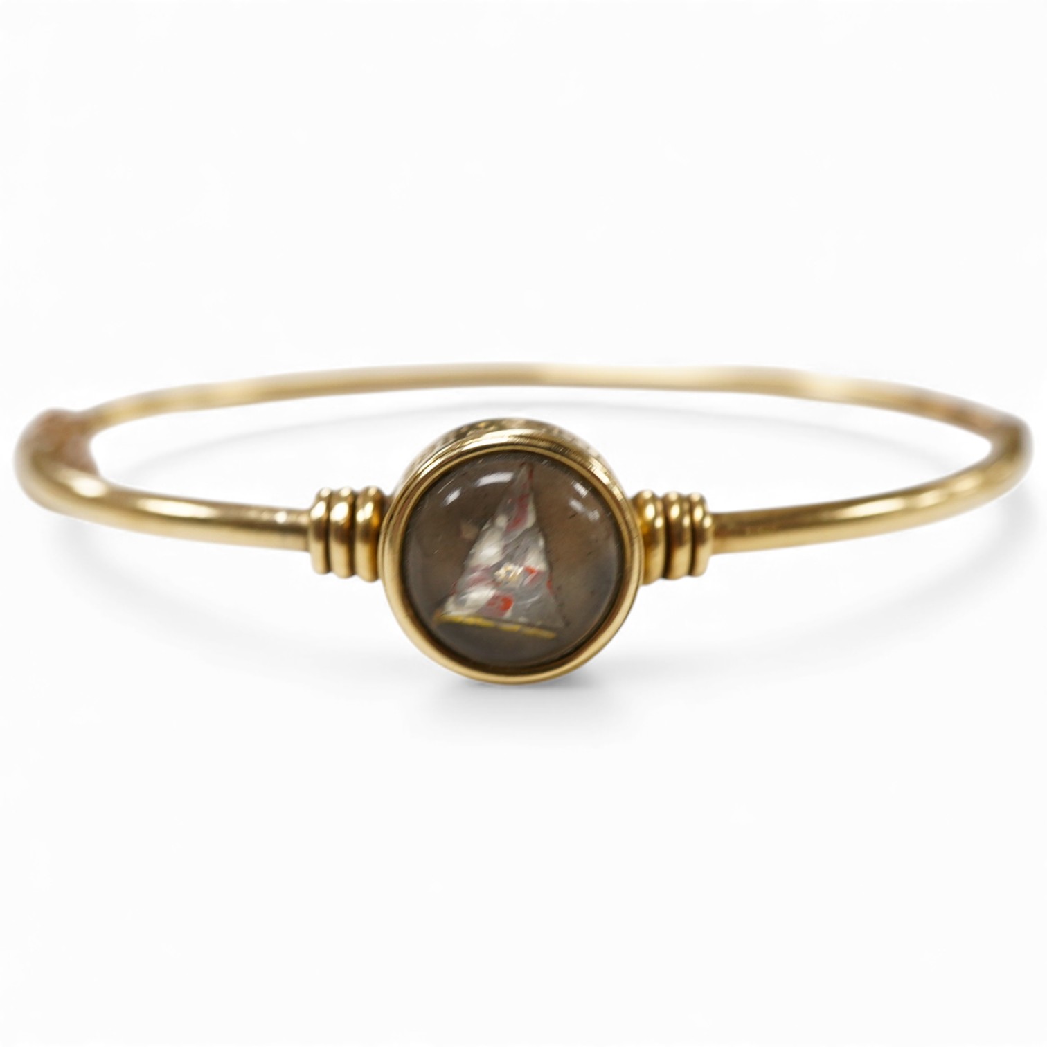 A regimental 'Essex Crystal' bangle, circa 1884, of hinged construction, collet-set with a reverse-carved and painted intaglio depicting the burgee of the Royal Yacht Squadron, mounted in gold, inscribed 'ER August 1884'